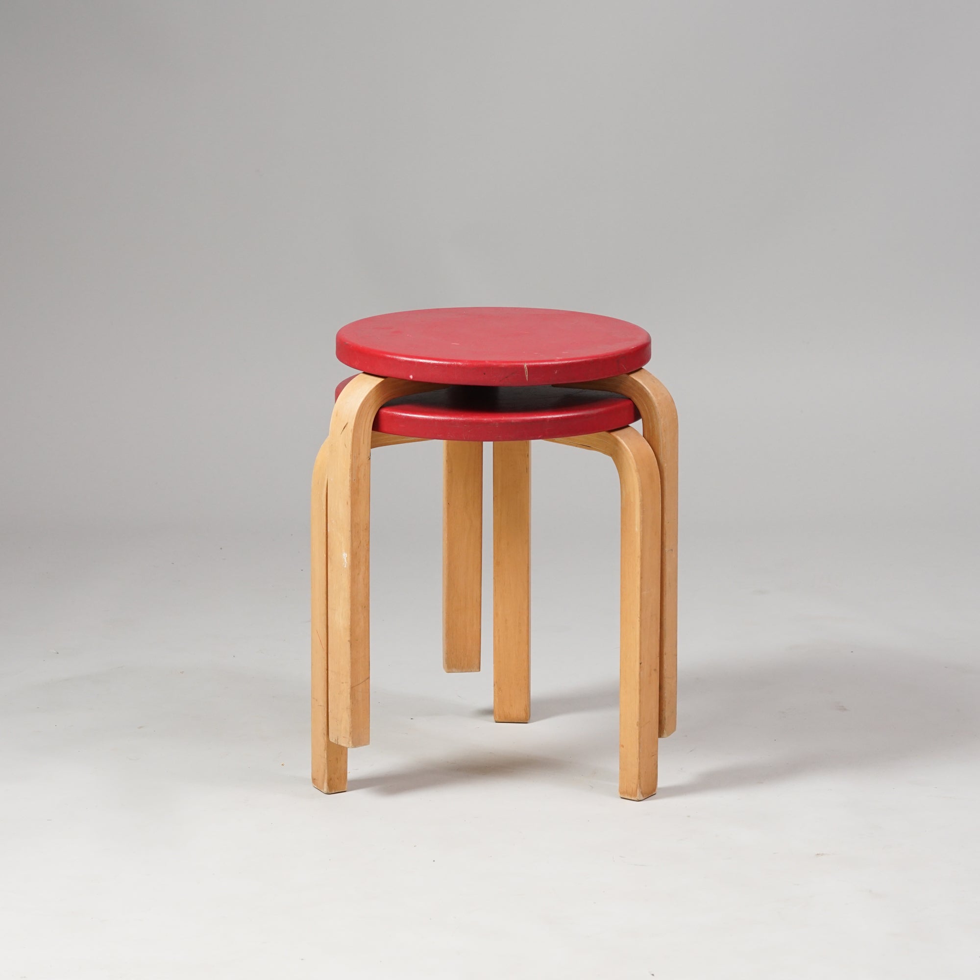 A stool with three legs and red round seat. Made of birch.