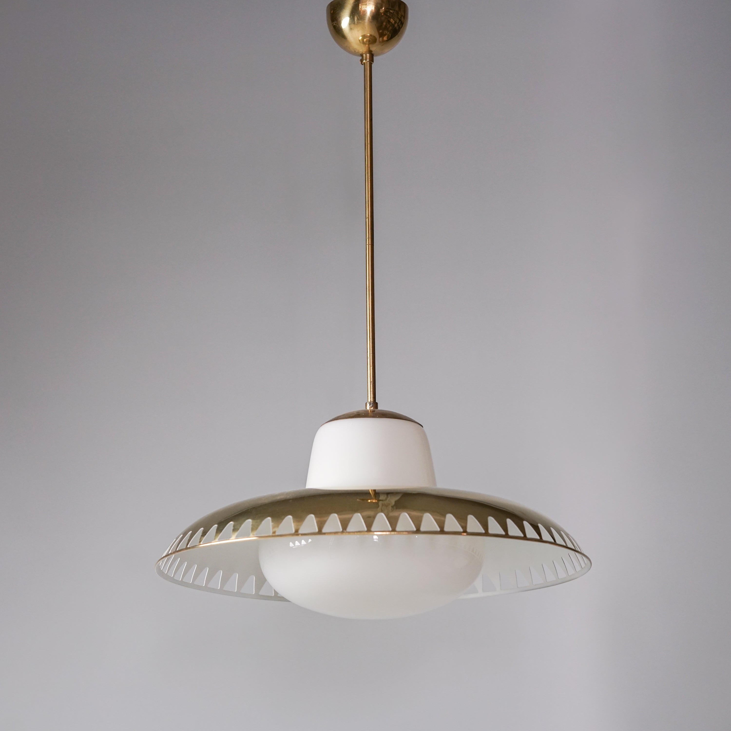 Pendant with white round glass dome in the middle. The glass bubble holds a brass shade  with a row of triangular holes along the edge.