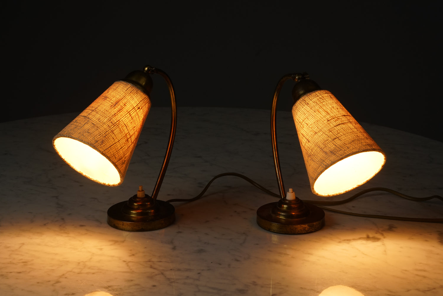 Table lamp with curved brass base and lampshade made of fabric. The white switch of the lamp is in middle of the base. 